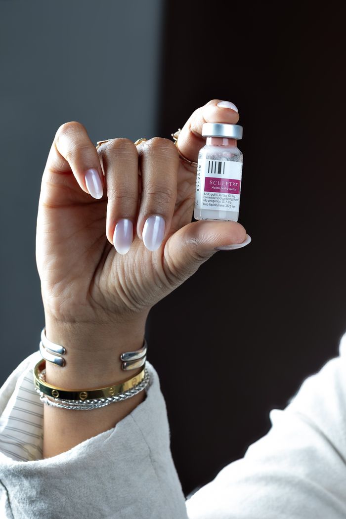 category-04 Detail of a person's hand holding a Sculptra cosmetic vial against a dark background.